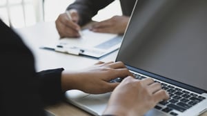 Hands typing on a laptop keyboard, diligently filling out an agent application form, depicting a focused and efficient task.