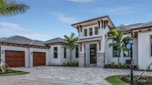 A high net worth-insured luxury home, framed by lush palm trees and featuring an impeccably designed brick driveway, epitomizing elegance.