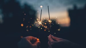 Two people holding half-burned sparklers together at dusk