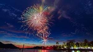 Red, white, and blue fireworks over water at dusk